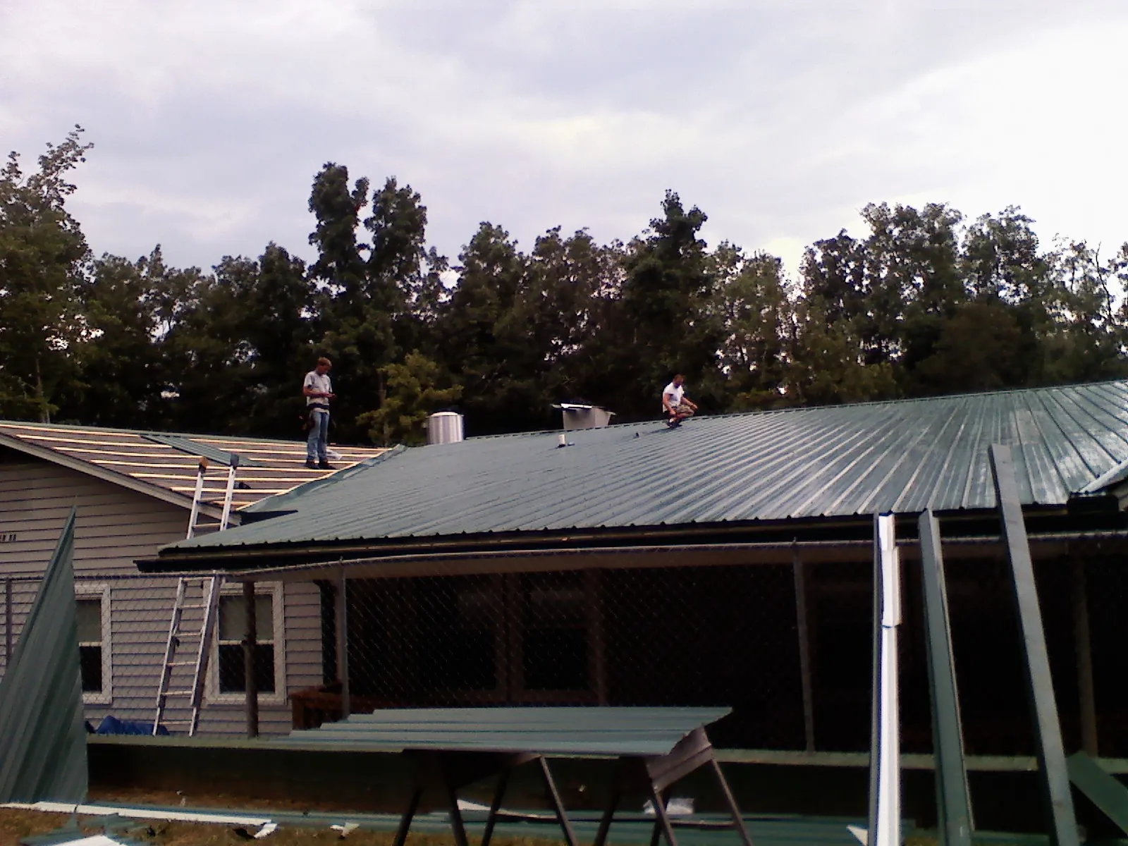 Two roofers installing green metal panels above a covered porch in Madison